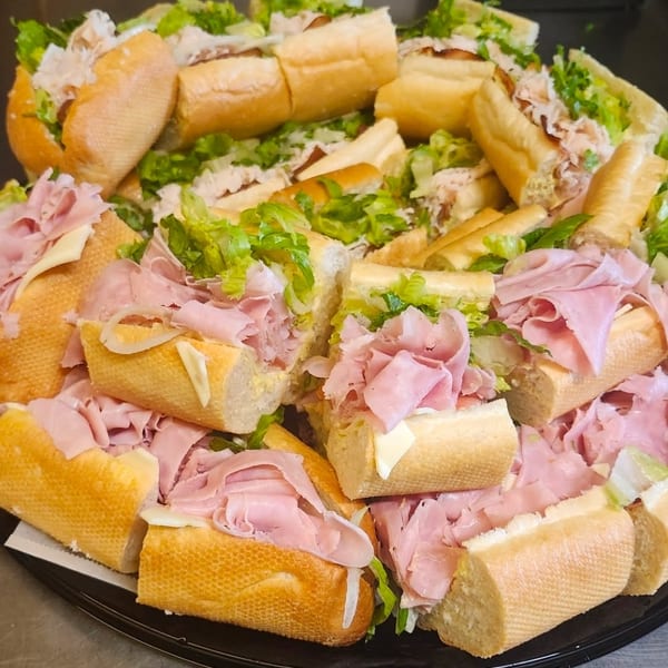 A platter of mini ham and turkey subs with lettuce, cheese, and onions.