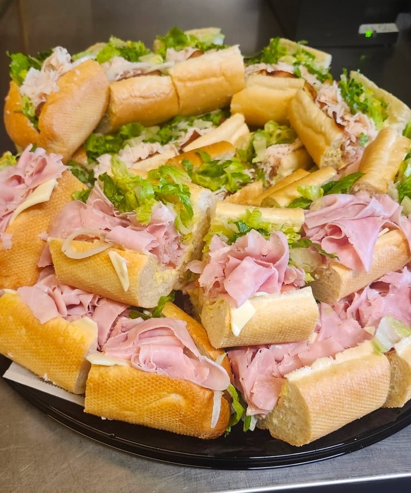 A platter of mini ham and turkey subs with lettuce, cheese, and onions.