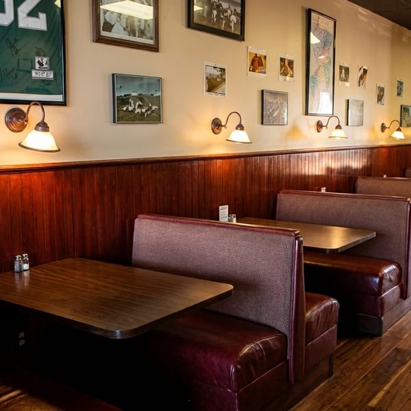 Empty restaurant interior with rows of brown leather booths, wooden tables, and wall decor.