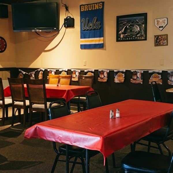 A casual restaurant dining room with red tablecloths, sports memorabilia, and a large TV screen.