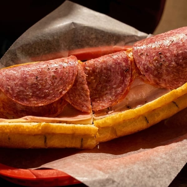 A large deli sub sandwich with salami, ham, and cheese on a red plate.