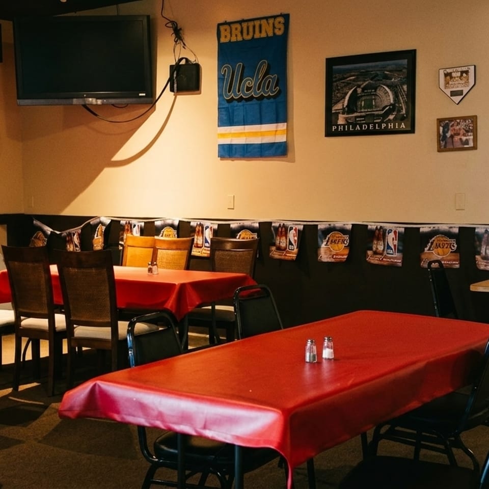 A dimly lit restaurant interior with red-covered tables, chairs, and sports memorabilia on the walls.