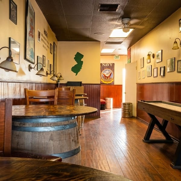 A long, narrow restaurant interior with wooden tables, chairs, and a shuffleboard table.